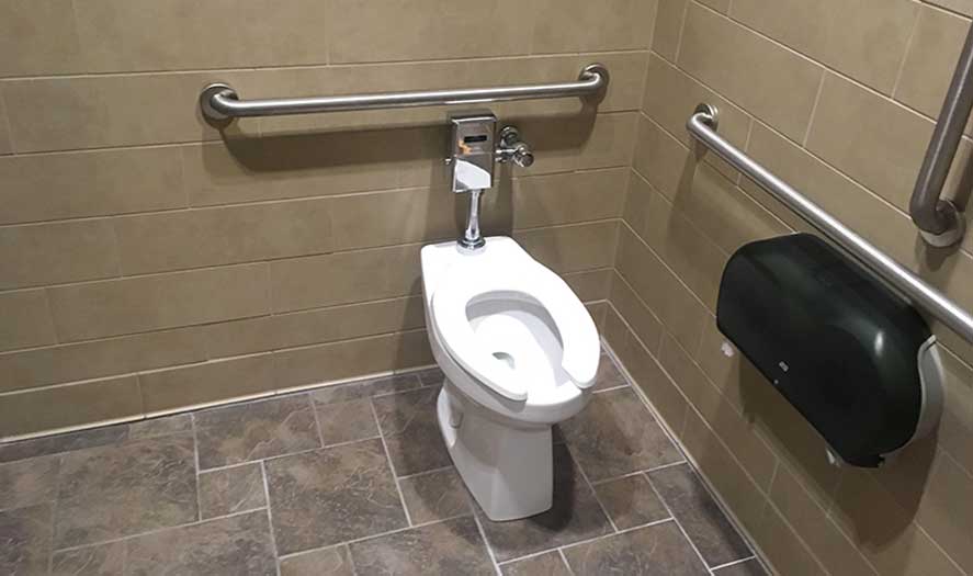 Accessible restroom with a white toilet, grab bars, and a paper towel dispenser, highlighting A & W Plumbing's commercial plumbing installations.