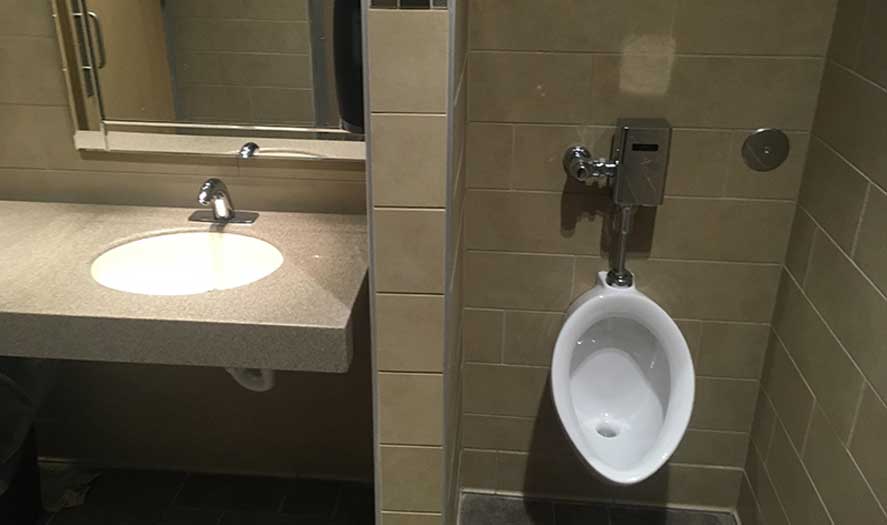 Commercial restroom with a modern sink and urinal, featuring tiled walls and a mirror, showcasing A & W Plumbing's installation work.