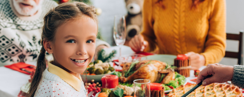 Young girl smiling at a holiday dining table with festive food, cozy decor, showcasing family celebration.