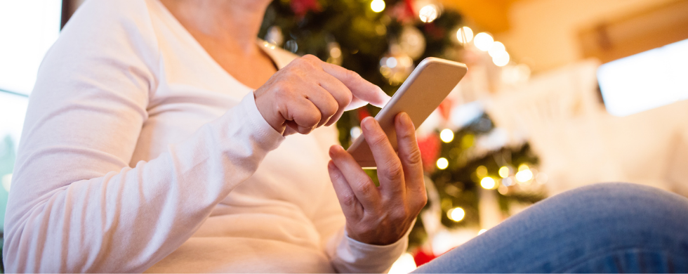 Person using smartphone in festive setting with Christmas tree, highlighting A & W Plumbing's holiday service offerings.