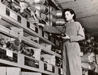 Lillian Ann Baumbach in a plumbing workshop, showcasing her pioneering role as the first woman master plumber, surrounded by plumbing supplies and materials.