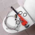 Plumbing tools, including an adjustable wrench and hoses, on a toilet in a clean bathroom. A & W Plumbing.