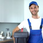 Technician in blue overalls with toolbox in a kitchen, offering plumbing services for water conservation. A & W Plumbing.
