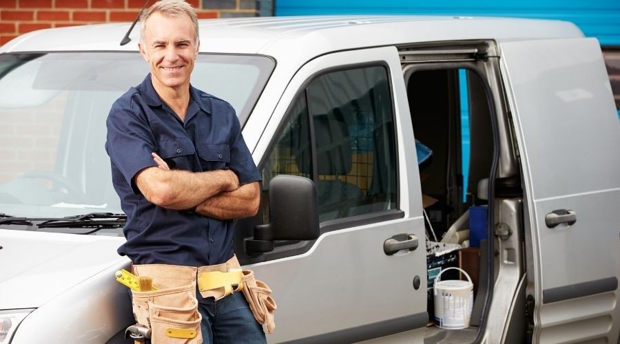 Male tradesperson in uniform with tool belt standing by A & W Plumbing and Heating work van door, showcasing supplies inside.