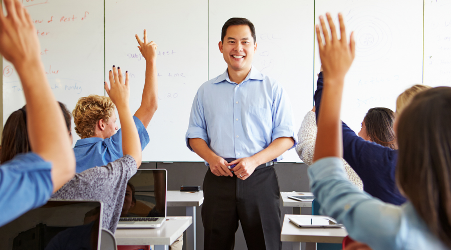 Teacher in classroom with students raising hands, showcasing engagement and learning at A & W Plumbing.