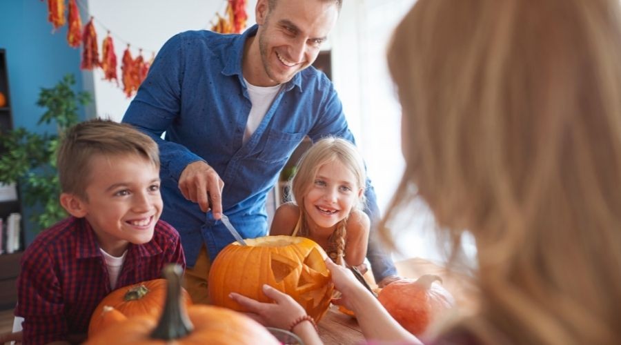 Two children and an adult carving pumpkins with tools, reflecting a joyful Halloween celebration for A & W Plumbing services.