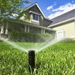 Residential sprinkler system on a green lawn under a clear blue sky, showcasing A & W Plumbing's water conservation efforts.