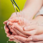 Two hands catching water flowing from a leaf, symbolizing plumbing and water conservation techniques.