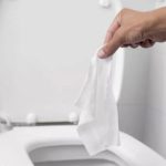 Hand holding a tissue in a clean, modern bathroom showing a toilet, representing A & W Plumbing and Heating's hygiene tips.