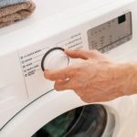 Eco-friendly washing machine control panel with settings, being adjusted by a hand.