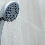 Chrome showerhead with water dripping in a modern bathroom, highlighting A & W Plumbing services.