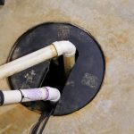 Sump pump installation with white PVC pipes connected to a black sump basin, highlighting essential home drainage equipment for preventing water damage.