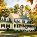 Charming two-story home with a welcoming porch, surrounded by trees and autumn foliage, representing a comfortable residence ideal for winter plumbing preparations.