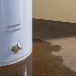 Leaking water heater tank with visible water pooling on the floor, highlighting the need for repair or replacement services from A & W Plumbing and Heating, Inc.