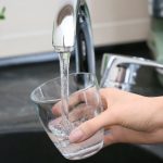 Hand filling a glass with clean water from a kitchen faucet, highlighting the importance of safe water supply and backflow prevention.