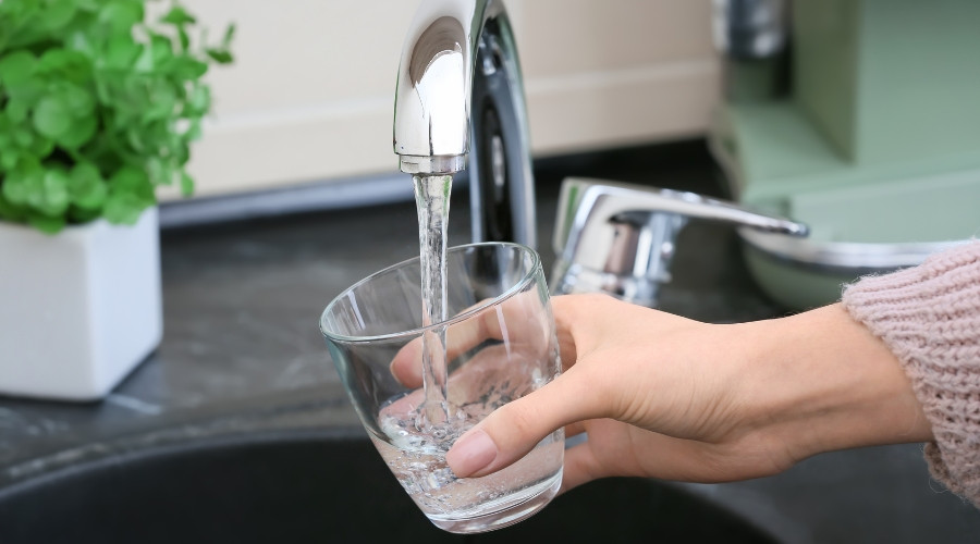 Hand holding a clear glass under a kitchen faucet, filling with water, demonstrating plumbing functionality and water quality.