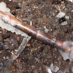 Copper plumbing fitting exposed in dirt, illustrating potential winter damage to exterior plumbing fixtures.