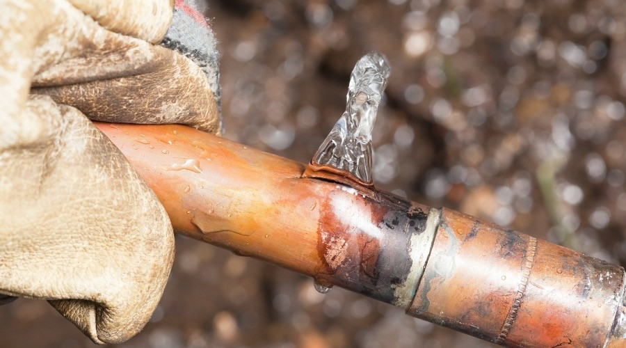 Close-up of a damaged copper pipe with water leaking, showcasing plumbing issues relevant to bathroom upgrades and repairs.
